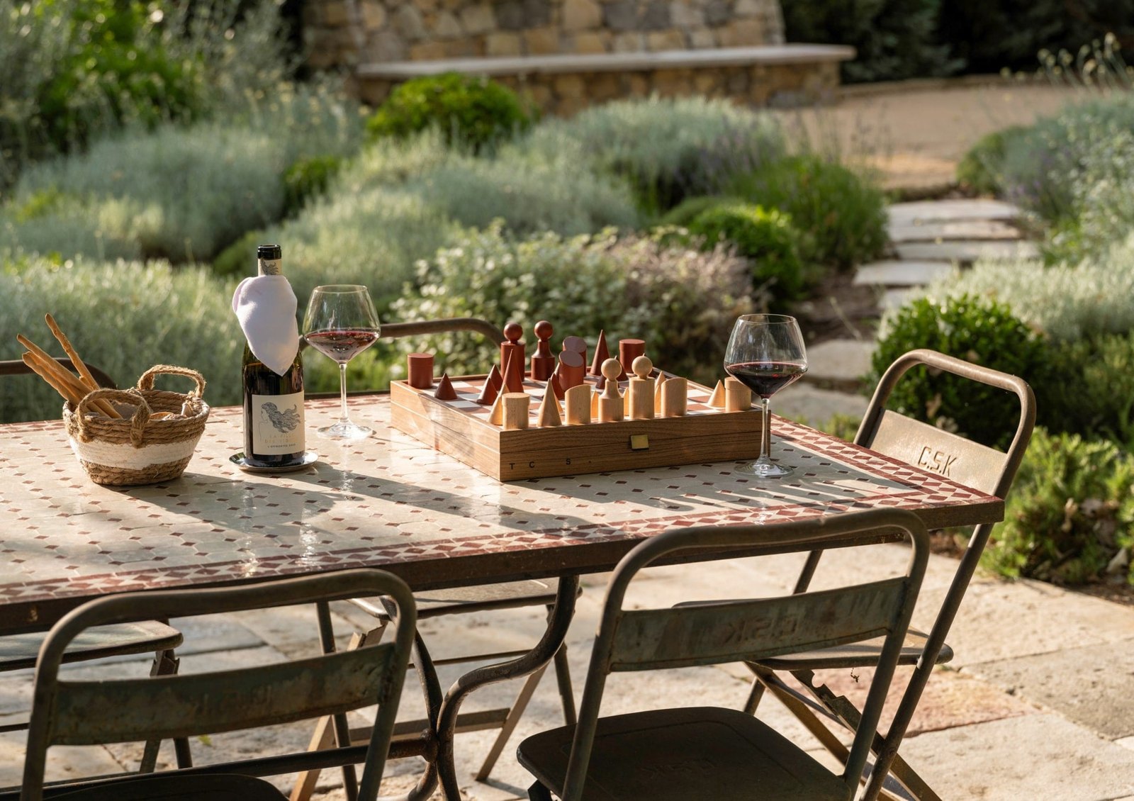 Chess, red wine and breadsticks on a mosaic table in a lavender garden