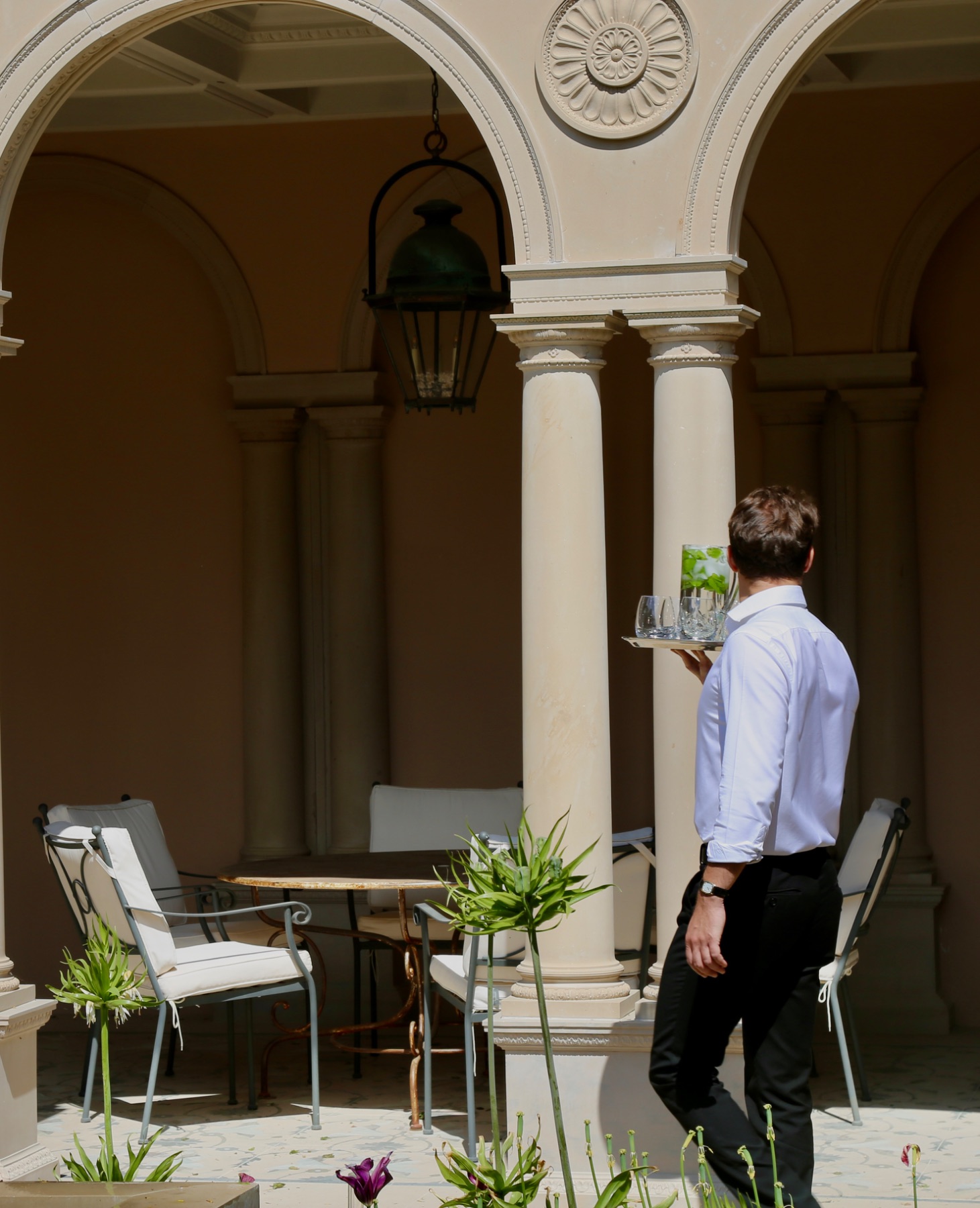 Staff in good company: a waiter in a white shirt carrying a tray of glasses through a stone courtyard