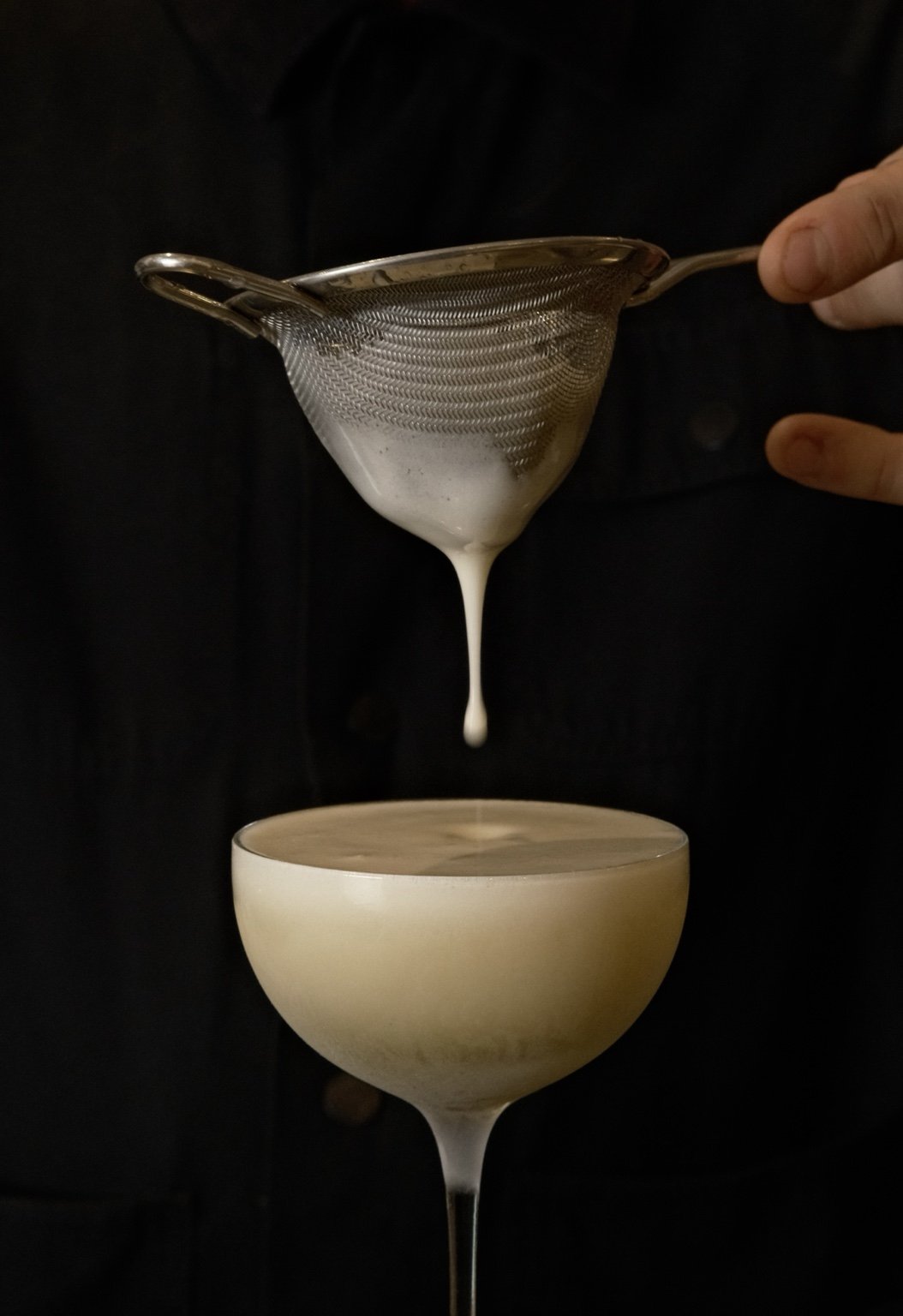 Private events: a bartender straining a pale foaming cocktail into a coupe