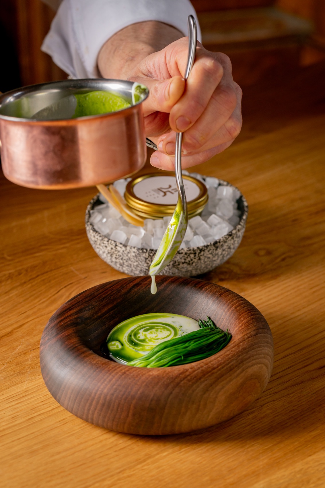 Private dining in London: a chef spooning a green sauce from a copper pan into a dark wooden bowl