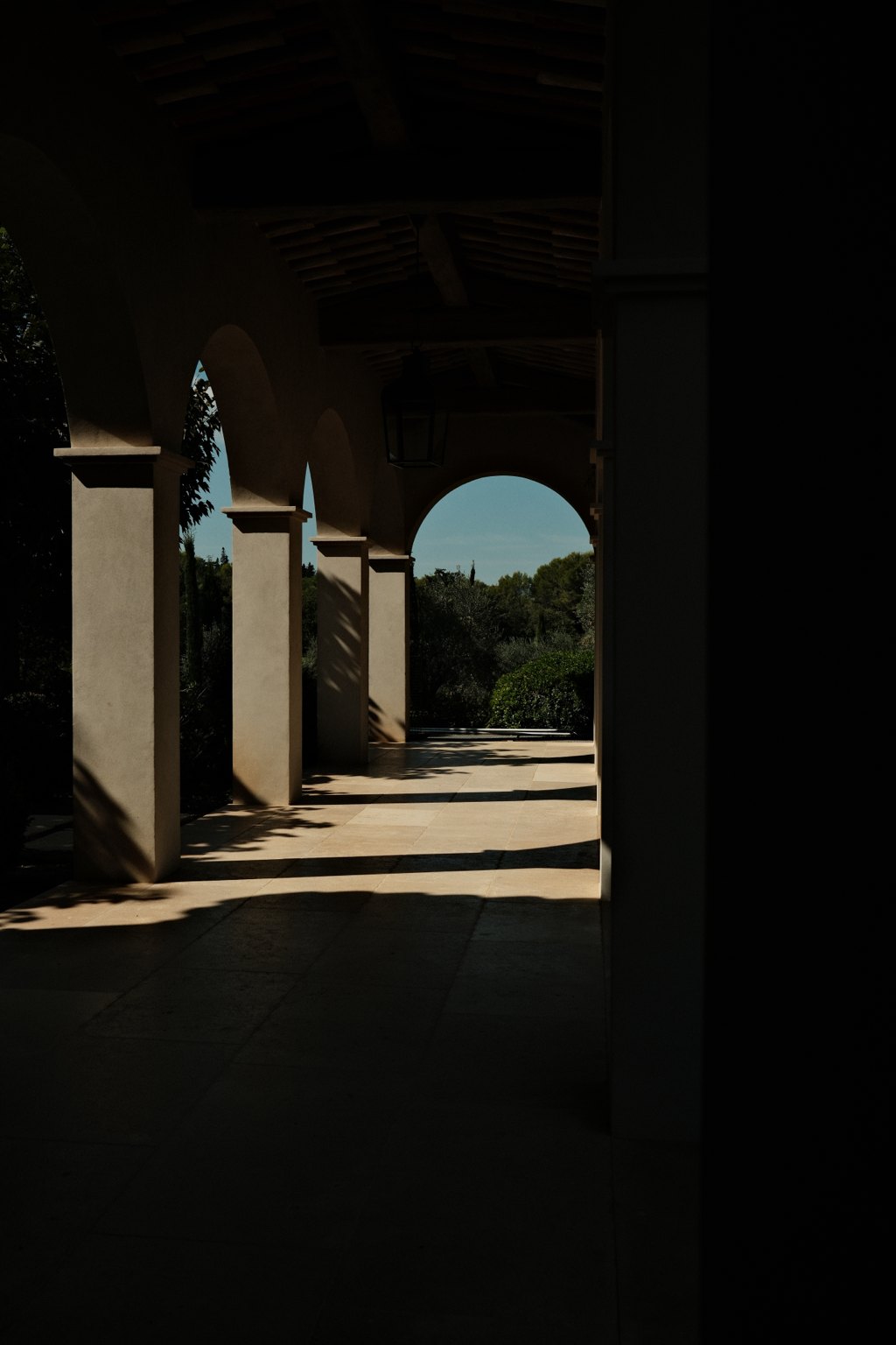 A shaded stone loggia of arches opening onto Provençal trees