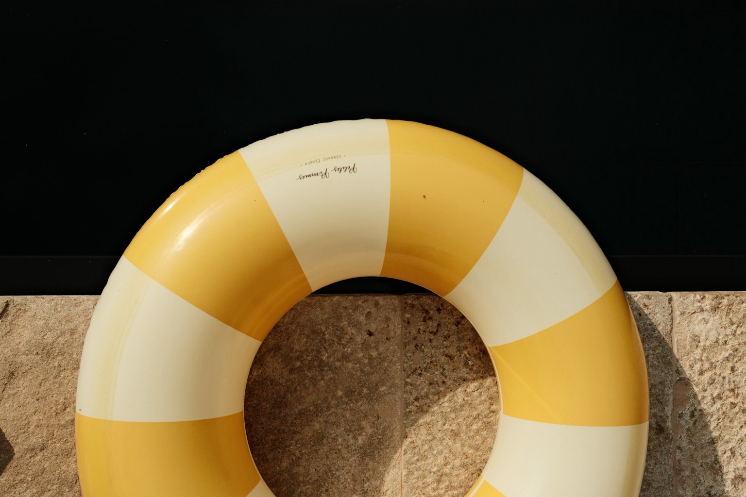 A yellow and white striped pool ring resting against warm stone