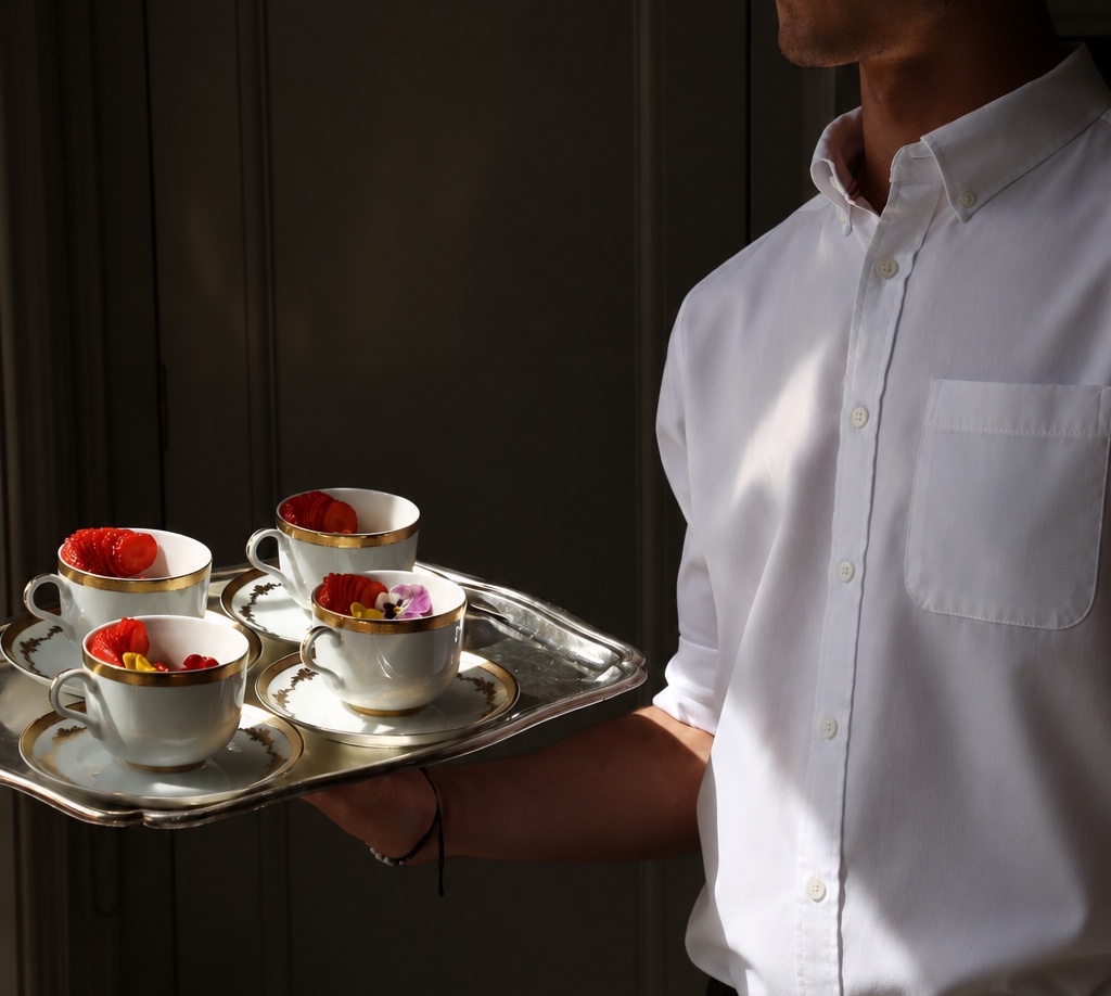 A waiter in shadow carrying a silver tray of porcelain cups